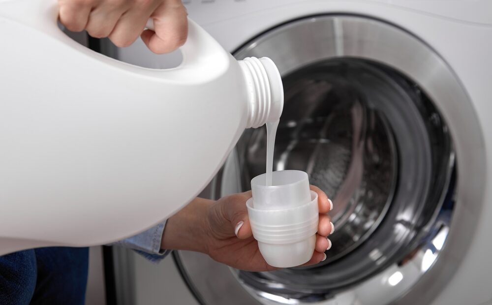 Against,Background,Of,Drum,Of,Steel colored,Washing,Machine,,Woman,Pours